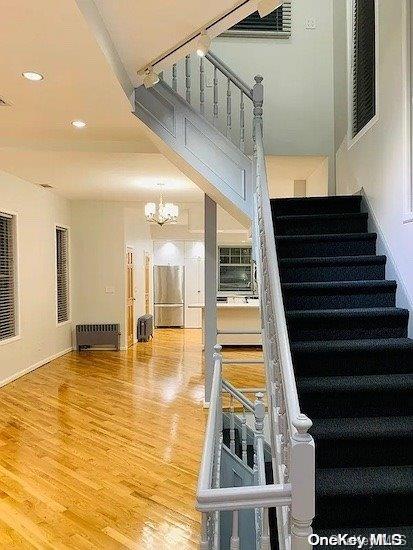 staircase featuring hardwood / wood-style flooring, radiator, and a chandelier