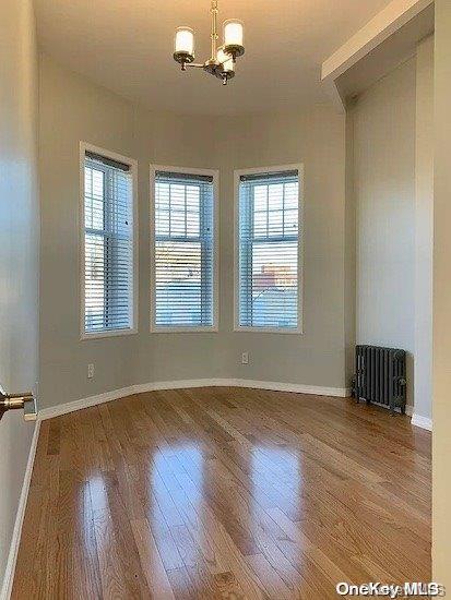 empty room featuring hardwood / wood-style floors, a notable chandelier, and radiator heating unit