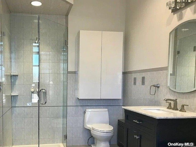 bathroom featuring vanity, a shower with door, toilet, and tile walls