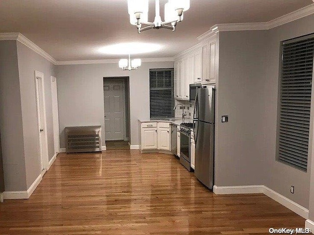 kitchen with wood-type flooring, stainless steel appliances, an inviting chandelier, and white cabinetry