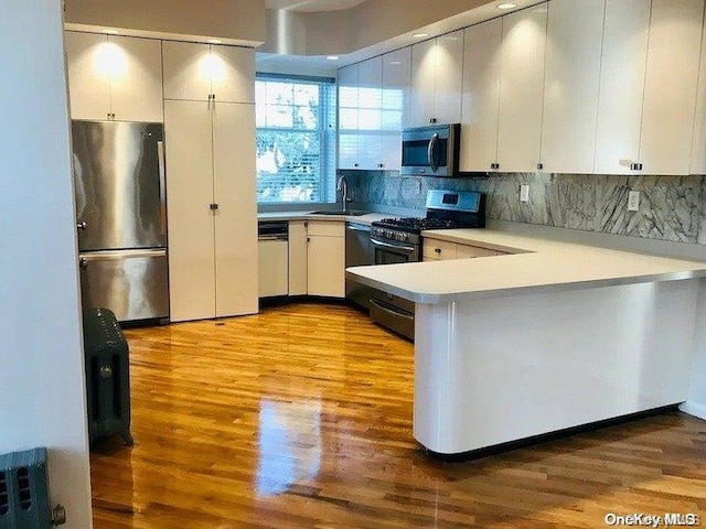 25-54 37th St, Astoria, NY 11103 - kitchen with appliances with stainless steel finishes, light wood-type flooring, light countertops, a peninsula, and backsplash