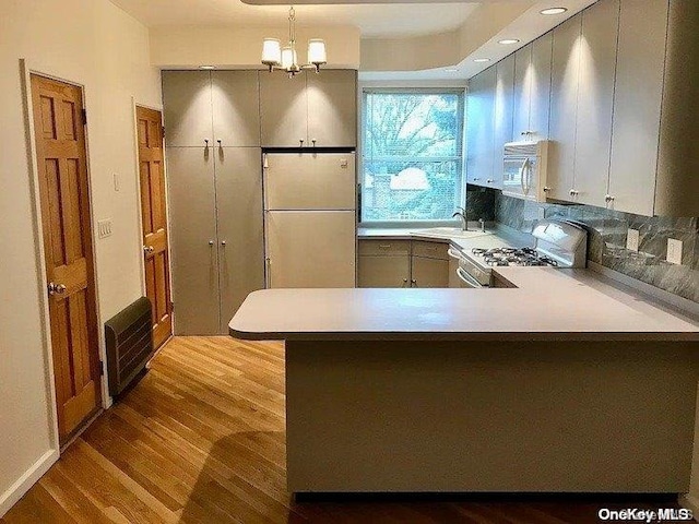 kitchen with a notable chandelier, kitchen peninsula, light hardwood / wood-style floors, decorative light fixtures, and white appliances