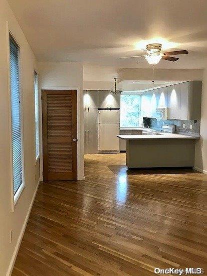 kitchen with kitchen peninsula, decorative backsplash, ceiling fan, and dark wood-type flooring