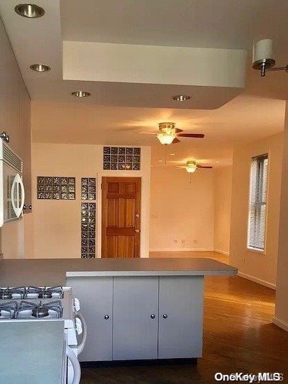 kitchen with dark hardwood / wood-style floors, ceiling fan, gas range oven, and kitchen peninsula