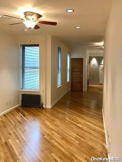 spare room featuring ceiling fan, radiator heating unit, and wood-type flooring