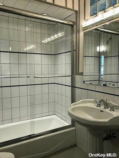 bathroom with tiled shower / bath combo, sink, and tile walls