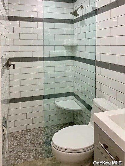 bathroom with toilet, a tile shower, tile walls, and vanity