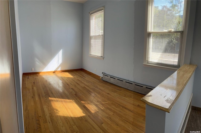 empty room with wood-type flooring, a wealth of natural light, and a baseboard heating unit