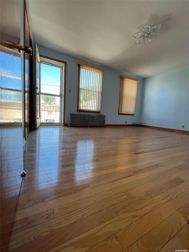 empty room featuring ceiling fan, light wood-type flooring, and radiator heating unit