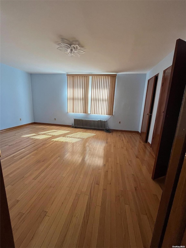 empty room featuring ceiling fan, light hardwood / wood-style floors, and radiator heating unit