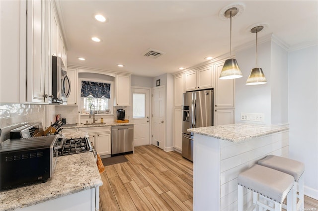 kitchen featuring pendant lighting, white cabinets, light hardwood / wood-style flooring, appliances with stainless steel finishes, and light stone counters