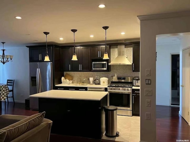 kitchen featuring decorative backsplash, stainless steel appliances, wall chimney range hood, a kitchen island, and hanging light fixtures