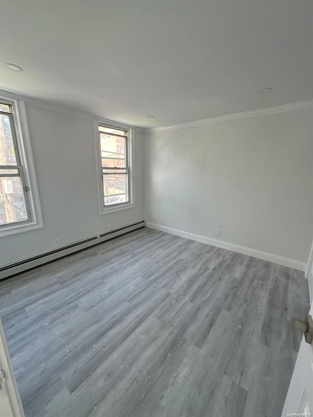 empty room featuring light hardwood / wood-style floors, ornamental molding, and a baseboard heating unit