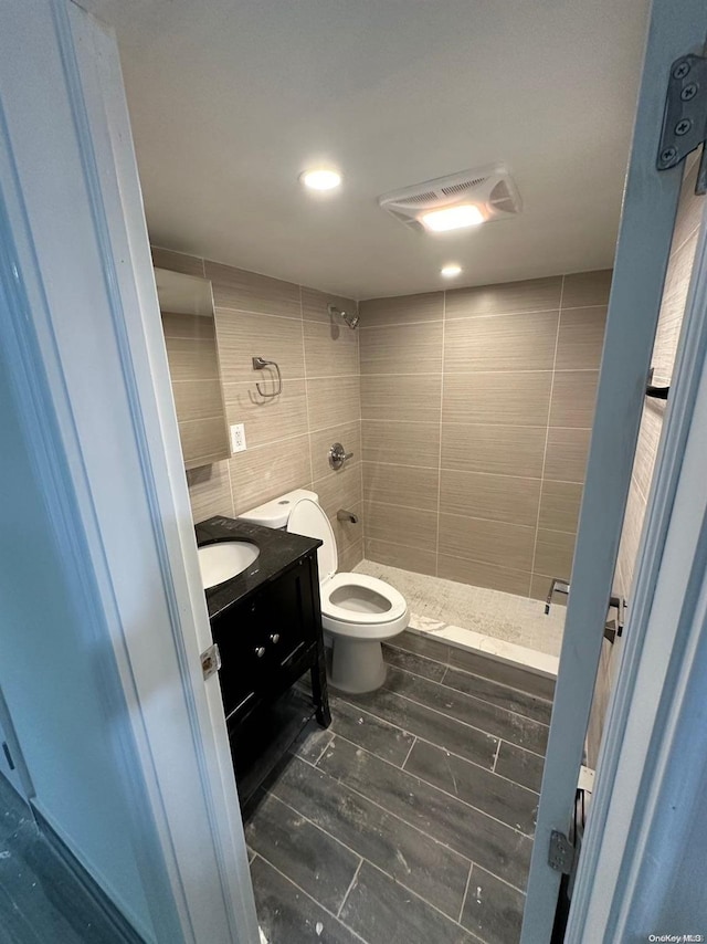 bathroom with a tile shower, vanity, tile walls, and toilet