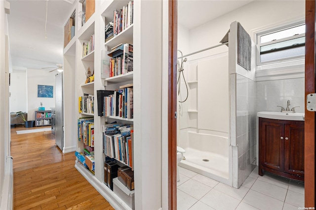 bathroom featuring vanity, a shower, hardwood / wood-style flooring, ceiling fan, and tile walls