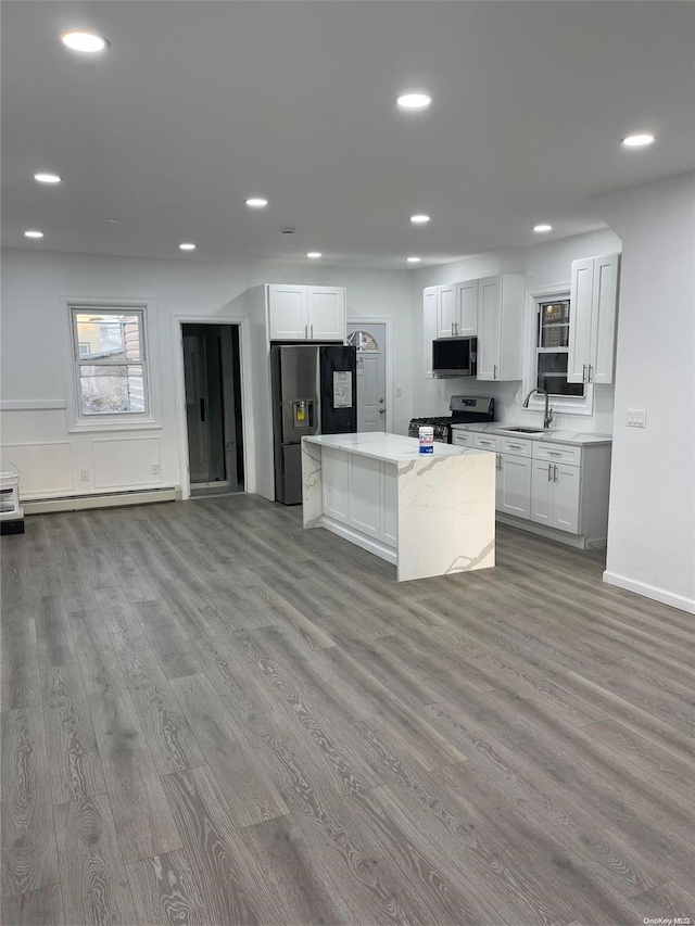 kitchen featuring light wood-type flooring, appliances with stainless steel finishes, a baseboard radiator, a kitchen island, and white cabinetry