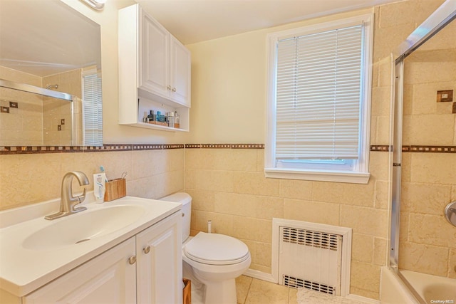 full bathroom featuring radiator heating unit, tile patterned flooring, combined bath / shower with glass door, vanity, and tile walls