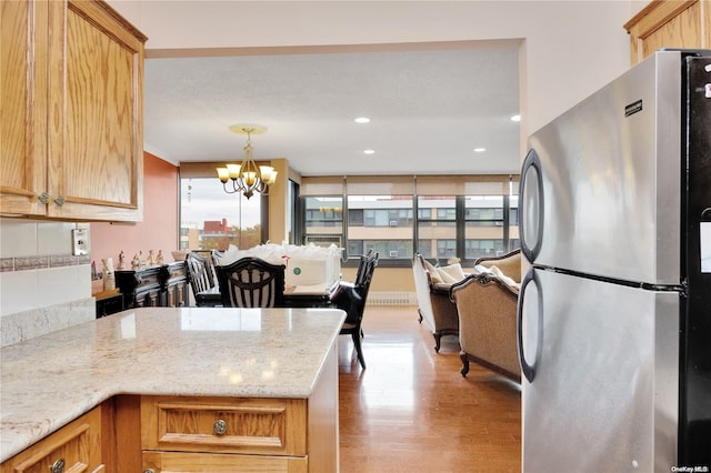 kitchen featuring stainless steel fridge, light stone counters, light wood-type flooring, and a chandelier