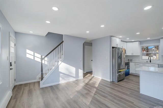 kitchen featuring backsplash, light hardwood / wood-style flooring, stainless steel fridge, a baseboard radiator, and white cabinetry