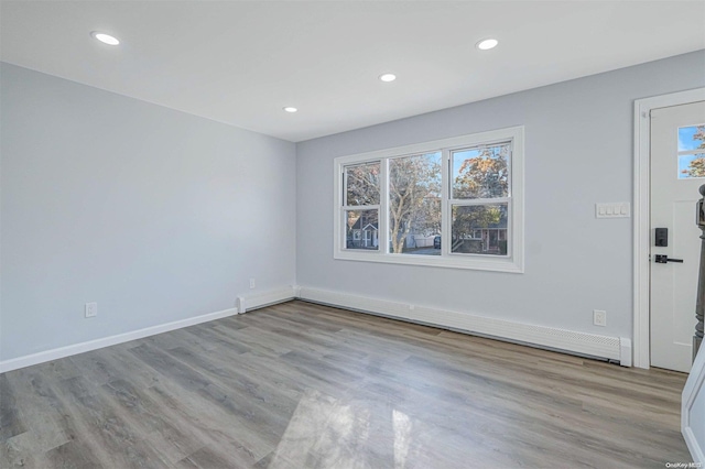 unfurnished room with light wood-type flooring, a baseboard radiator, and a wealth of natural light