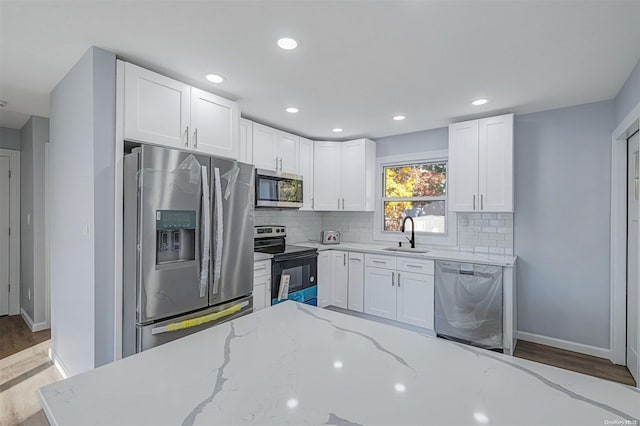 kitchen with white cabinetry, light stone counters, stainless steel appliances, and hardwood / wood-style flooring