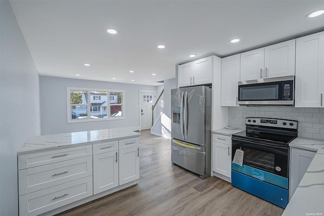 kitchen featuring backsplash, white cabinets, light stone countertops, light wood-type flooring, and stainless steel appliances