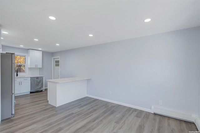 kitchen with kitchen peninsula, appliances with stainless steel finishes, a baseboard heating unit, light hardwood / wood-style flooring, and white cabinets