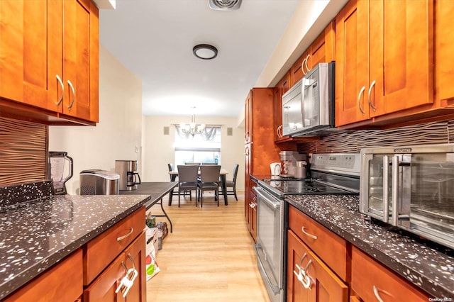 kitchen featuring appliances with stainless steel finishes, light wood-type flooring, dark stone counters, pendant lighting, and a chandelier