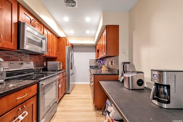 kitchen featuring sink, tasteful backsplash, light hardwood / wood-style flooring, dark stone counters, and appliances with stainless steel finishes