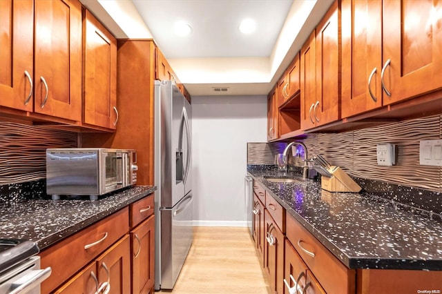 kitchen with decorative backsplash, appliances with stainless steel finishes, dark stone counters, sink, and light hardwood / wood-style floors