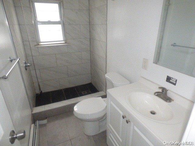 bathroom featuring tiled shower, tile patterned flooring, vanity, and toilet