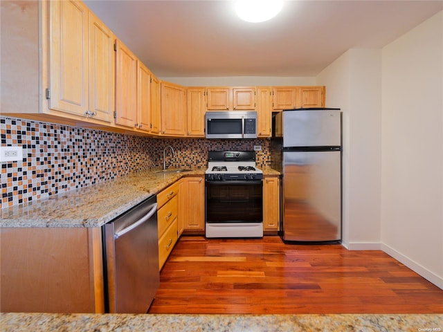 kitchen featuring backsplash, light stone counters, light hardwood / wood-style floors, and appliances with stainless steel finishes