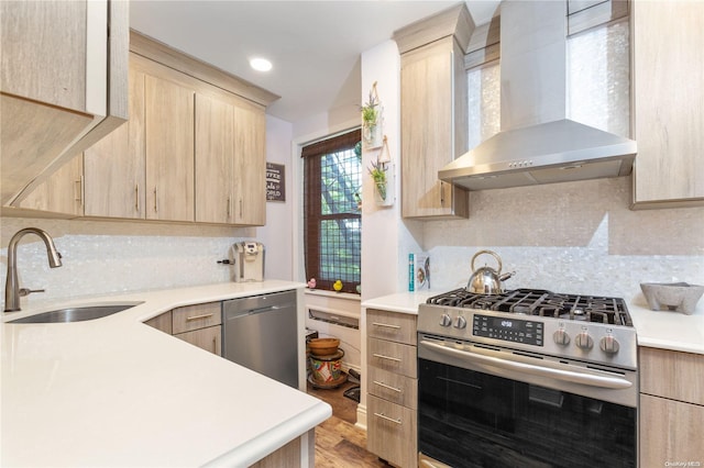 kitchen with sink, light brown cabinets, wall chimney range hood, light hardwood / wood-style flooring, and appliances with stainless steel finishes