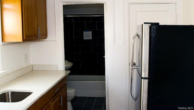 kitchen with sink, dark tile patterned flooring, tasteful backsplash, and stainless steel fridge