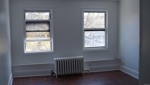 empty room with a wealth of natural light, dark parquet floors, and radiator