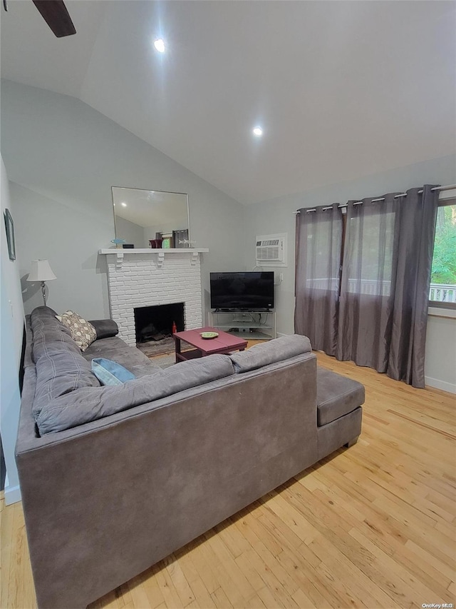 living room with a wall mounted air conditioner, lofted ceiling, a brick fireplace, ceiling fan, and light wood-type flooring