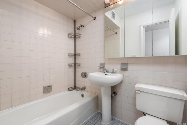 bathroom featuring tile patterned floors, tiled shower / bath, toilet, tile walls, and tasteful backsplash