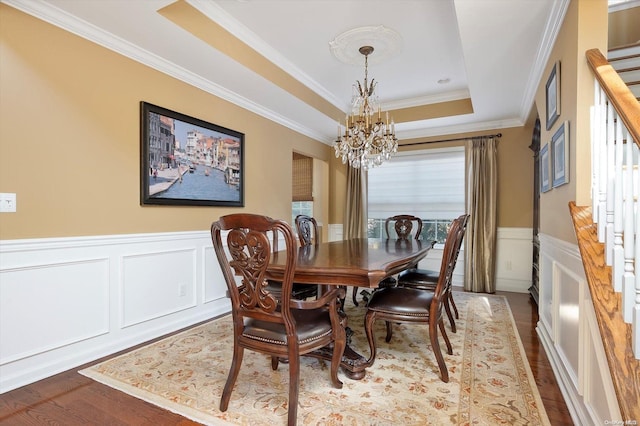 dining room featuring a tray ceiling, hardwood / wood-style floors, ornamental molding, and a notable chandelier