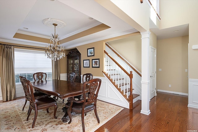 dining room featuring an inviting chandelier, a raised ceiling, crown molding, dark hardwood / wood-style flooring, and decorative columns