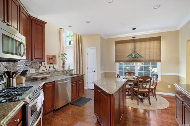 kitchen featuring dark wood-type flooring, stainless steel appliances, hanging light fixtures, and a healthy amount of sunlight