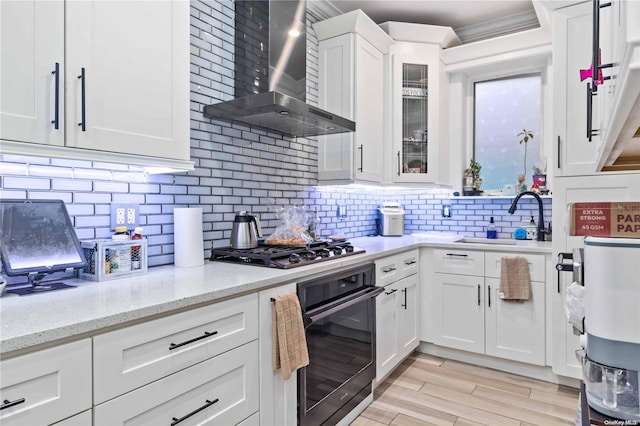 kitchen featuring sink, stainless steel appliances, wall chimney range hood, decorative backsplash, and white cabinets