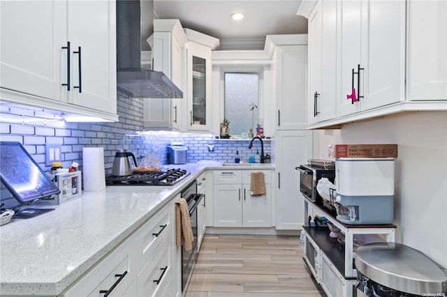 kitchen with sink, wall chimney exhaust hood, light hardwood / wood-style floors, white cabinets, and black appliances