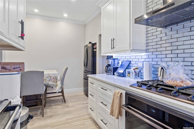 kitchen featuring wall chimney range hood, decorative backsplash, light hardwood / wood-style floors, white cabinetry, and stainless steel appliances