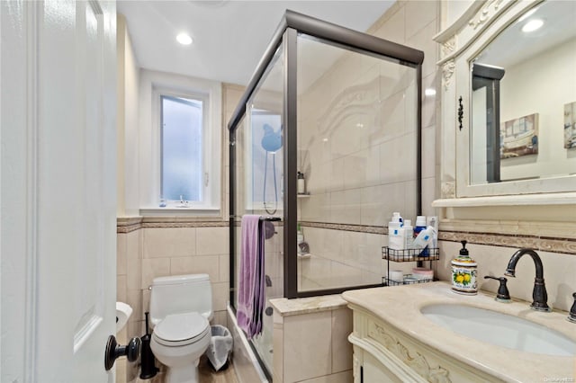 bathroom with a shower with door, vanity, tile walls, and toilet