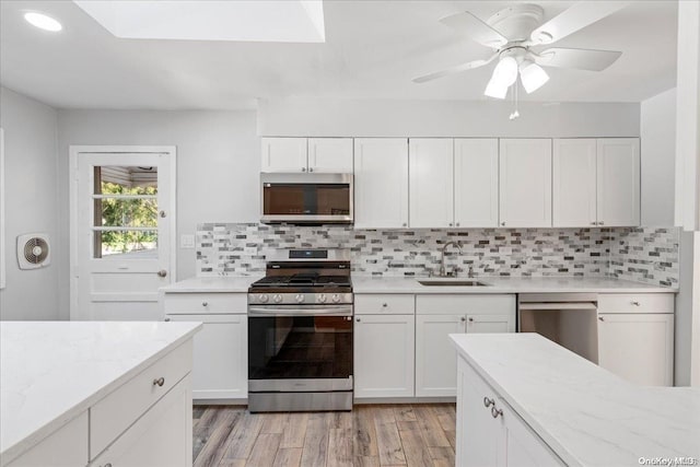 kitchen featuring sink, light hardwood / wood-style floors, decorative backsplash, white cabinets, and appliances with stainless steel finishes