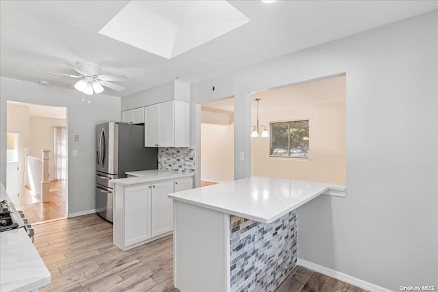 kitchen with kitchen peninsula, stainless steel fridge, light wood-type flooring, white cabinetry, and a breakfast bar area