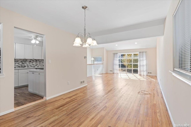 unfurnished dining area featuring ceiling fan with notable chandelier, light hardwood / wood-style floors, and sink