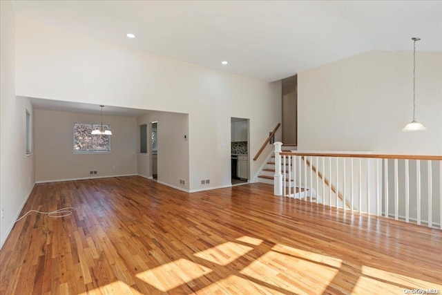 unfurnished living room with wood-type flooring, high vaulted ceiling, and a notable chandelier