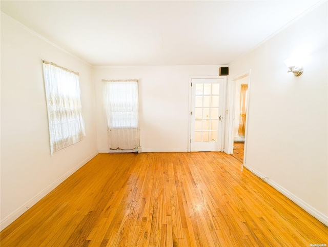 empty room with ornamental molding, baseboard heating, and light hardwood / wood-style flooring