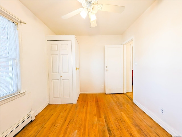 unfurnished bedroom featuring light wood-type flooring, a closet, ceiling fan, and a baseboard heating unit